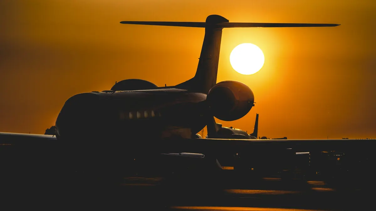 A private jet silhouetted against an orange evening sky